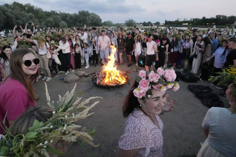Ukrainians gather around fire for a traditional Ukrainian celebration of Kupala Night, in Warsaw, Poland, on Saturday, June 22, 2024. Ukrainians in Warsaw jumped over a bonfire and floated braids to honor the vital powers of water and fire on the Vistula River bank Saturday night, as they celebrated their solstice tradition of Ivan Kupalo Night away from war-torn home. (AP Photo/Czarek Sokolowski)