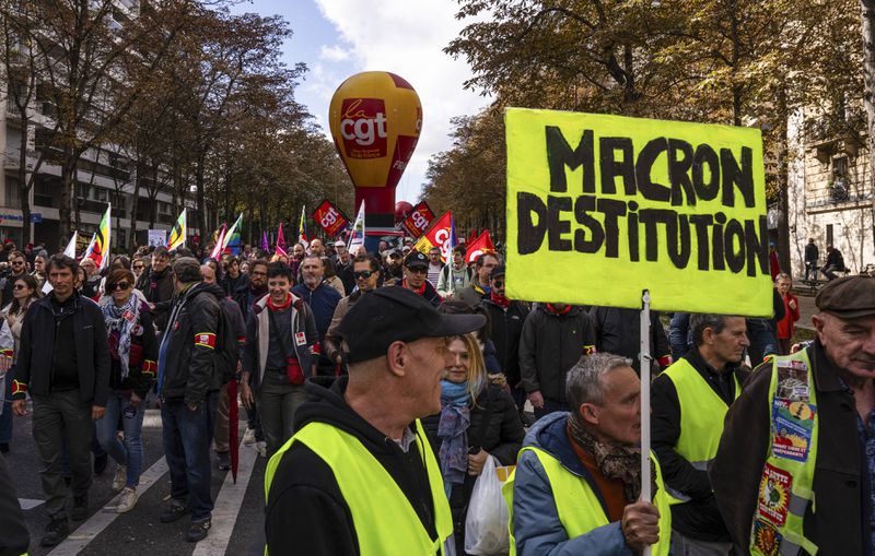 A protester holds a placard that reads, "Macron impeachment" during a rally against the new government of French Prime Minister Michel Barnier, in Paris, Tuesday, Oct. 1, 2024. (AP Photo/Louise Delmotte)