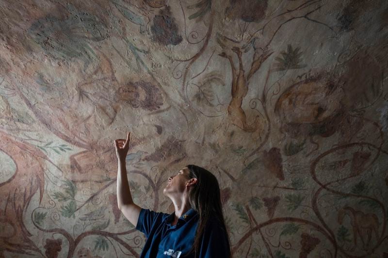 A worker points to an ancient wall of the archeological tomb site in Ashkelon, Israel, Tuesday, Aug. 27, 2024. The tomb with wall paintings depicting Greek mythological figures is at least 1,700 years old said the Israeli Antiquities Authority, whose workers are restoring the site. (AP Photo/Ohad Zwigenberg)