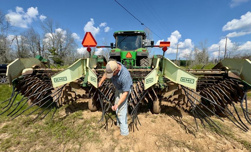 Peanut farmer Riley Davis inspects an attachment on his tractor, an implement known as a digger or a shaker. The long-pronged machinery is also referred to as an inverter. It uproots rows of mature peanuts, flipping them out of the ground to dry. (Joe Kovac Jr./AJC)