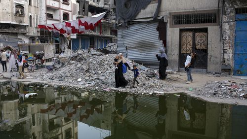 FILE - Palestinians displaced by the Israeli air and ground offensive on the Gaza Strip walk next a dark streak of sewage flowing into the streets of the southern town of Khan Younis, Gaza Strip, Thursday, July 4, 2024. Health authorities and aid agencies are racing to avert an outbreak of polio in the Gaza Strip after the virus was detected in the territory's wastewater and three cases with a suspected polio symptom have been reported. (AP Photo/Jehad Alshrafi, File)