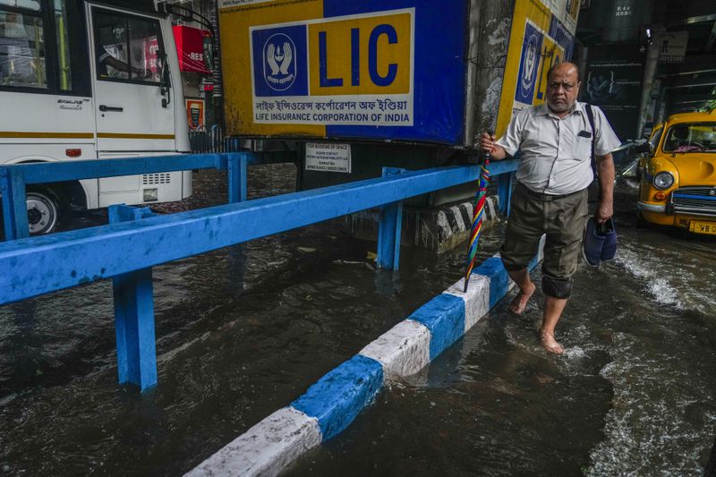 A man crosses a waterlogged street in Kolkata, India, as rain continues after cyclone Remal made a landfall near Bangladesh-India border, Monday, May 27, 2024. (AP Photo/Bikas Das)