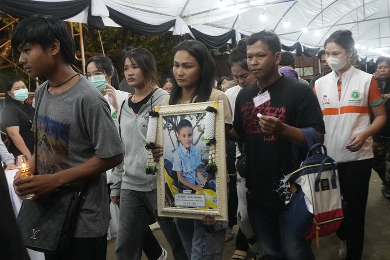 Victims' relatives carry portraits of the victims of a bus fire in a procession at Wat Khao Phraya Sangkharam School Lan Sak , Uthai Thani province, Thailand, Thursday, Oct. 3, 2024. (AP Photo/Sakchai Lalit)