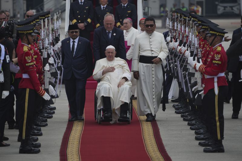 Pope Francis on his wheelchair, is welcomed as Indonesian Minister of Religious Affairs Yaqut Cholil Qoumas, center left, walks during an official welcoming ceremony at Soekarno-Hatta International Airport in Tangerang on the outskirts of Jakarta, Indonesia, Tuesday, Sept. 3, 2024. (AP Photo/Achmad Ibrahim)