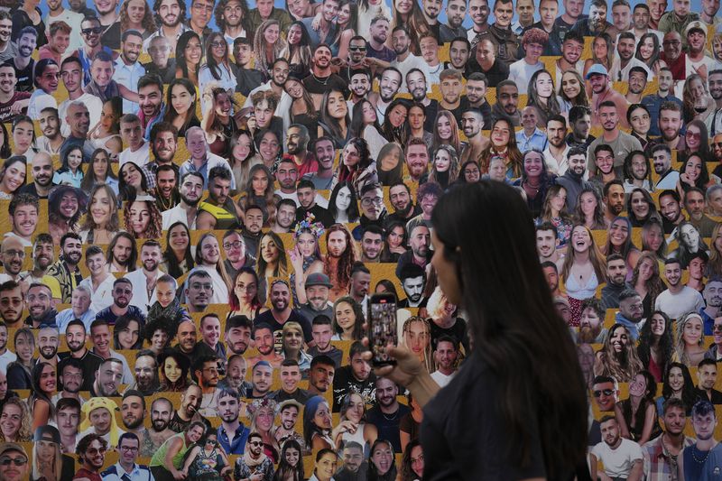 An attendant walks through a mural with portraits of the victims at the site of the Nova music festival, where hundreds of revelers were killed and abducted by Hamas and taken into Gaza, on the one-year anniversary of the attack, near Kibbutz Reim, southern Israel, Monday, Oct. 7, 2024. (AP Photo/Ariel Shalit)