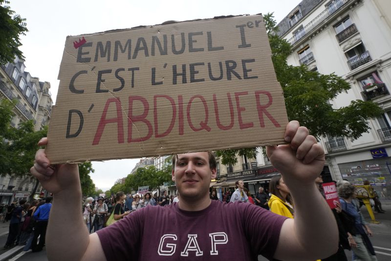 A demonstrator holds a placard which reads 'Emmanuel it's time to abdicate' during a protest, responding to a call from the far-left party who criticized as a power grab the president's appointment of a conservative new prime minister, Michel Barnier, in Paris, France, Saturday, Sept. 7, 2024. (AP Photo/Michel Euler)