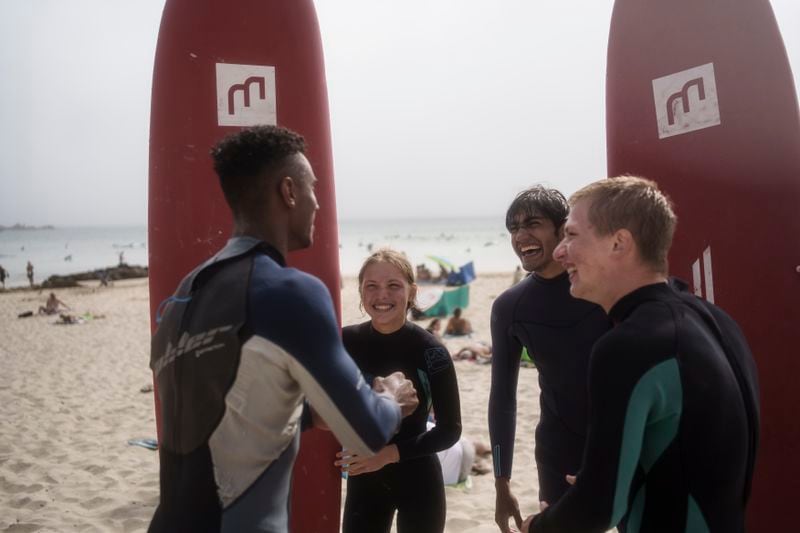 Uliana Yarova, center, laughs while on a break from surfing with other members of Surf Church Church in Matosinhos beach in the suburbs of Porto, Portugal on Sunday, Aug. 18, 2024. The Ukrainian teenager fled her war-torn country with her family after Russia's invasion and found refuge in Porto and Surf Church. (AP Photo/Luis Andres Henao)