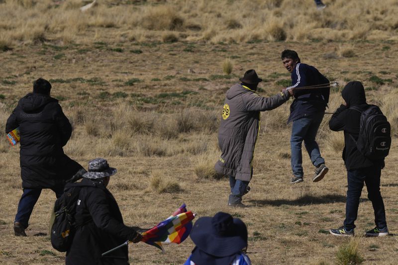 Supporters of former President Evo Morales, one holding a sling-shot, pursue a government supporter, top right, in Vila Vila, Bolivia, as they march to the capital, Tuesday, Sept. 17, 2024. Morales and his supporters are marching to the capital to protest the government of President Luis Arce in an escalation of a political dispute between the two politicians. (AP Photo/Juan Karita)