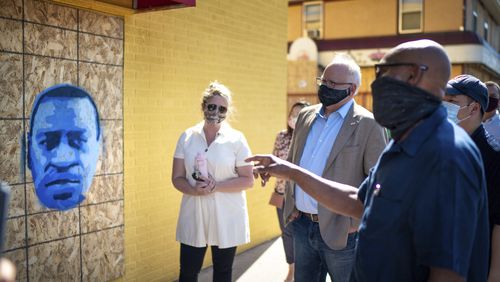 FILE - Minnesota Gov. Tim Walz, center right, listens to artist Seitu Jones, right, talk about his stencil of George Floyd, in St. Paul, Minn., Monday, June 8, 2020. (Glen Stubbe/Star Tribune via AP, Pool)