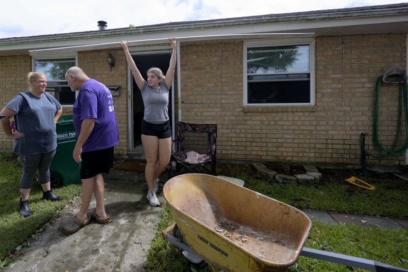 Kelsie Schmidt, right, walks a board to a debris pile from her family's home after floodwater came up a few inches in the house making most of the walls, floors, and doors wet after Hurricane Francine in Kenner, La., in Jefferson Parish, Thursday, Sept. 12, 2024. (AP Photo/Matthew Hinton)