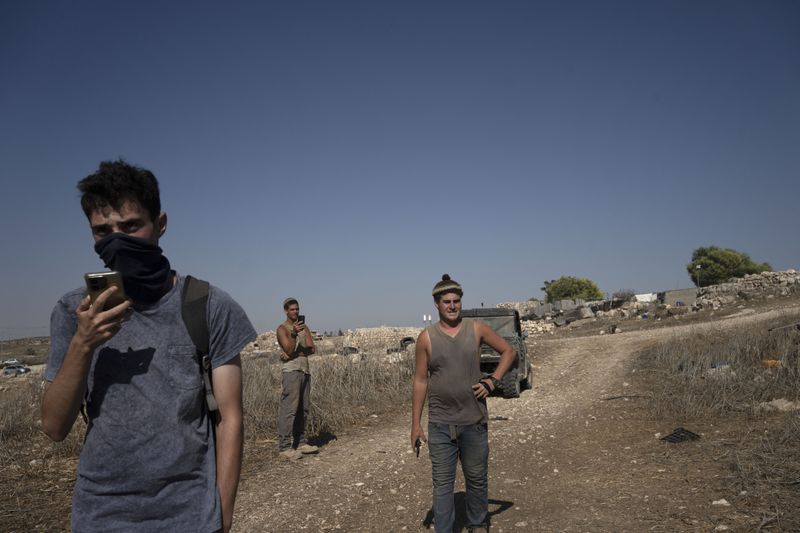 An Israeli activist, left, calls Israeli Police as settlers visit the West Bank village of Khirbet Zanuta, Thursday, Aug. 29, 2024. Ten months after settlers threatened to kill them if they didn't leave their village, some Palestinian residents are finally home, under a rare court order. (AP Photo/Maya Alleruzzo)