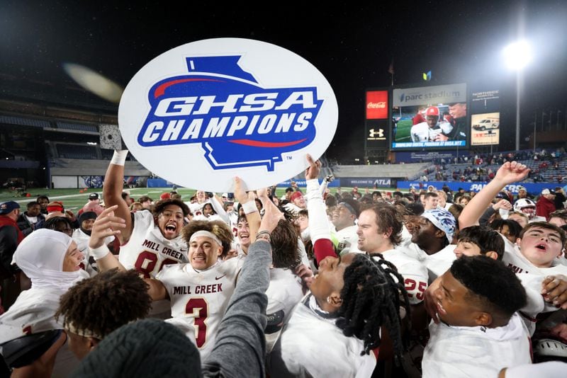 Mill Creek’s Nick Maxey (88), Trajen Green (3) and teammates host the GHSA Champions sign after their 70-35 win against Carrollton in the GHSA Class 7A finals, at Center Parc Stadium, Saturday, December 10, 2022, in Atlanta. (Jason Getz / Jason.Getz@ajc.com)