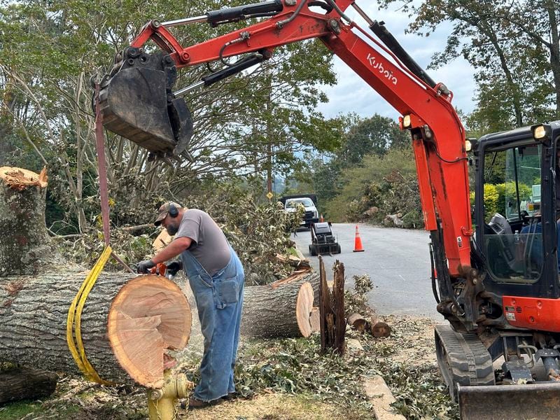 A worker cuts up a tree that impaled itself on a fire hydrant during Hurricane Helene, Friday, Oct. 4, 2024, in the Oak Forest neighborhood of Asheville, N.C. (AP Photo/Jeff Amy)