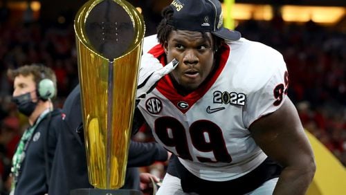 Georgia Bulldogs defensive lineman Jordan Davis looks at himself in the reflection of the trophy after UGA's 33-18 win against the Alabama Crimson Tide at the 2022 College Football Playoff National Championship on Jan. 10 at Lucas Oil Stadium in Indianapolis.  (Curtis Compton / Curtis.Compton@ajc.com)