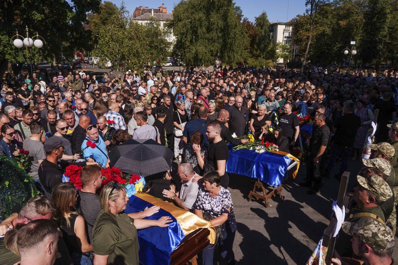 Relatives and friends mourn near the coffins of six Ukrainian servicemen killed in a Russian rocket attack at a Ukrainian military academy, during their funeral ceremony in Poltava, Ukraine, Saturday Sept. 7, 2024. (AP Photo/Evgeniy Maloletka)