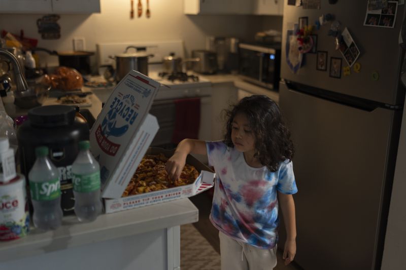 Rubie Caceres, a granddaughter of Marina Maalouf, a longtime resident of Hillside Villa, grabs a slice of pizza in her apartment in Los Angeles, Tuesday, Oct. 1, 2024. (AP Photo/Jae C. Hong)