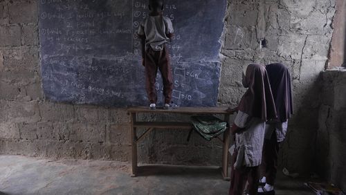 Students of Excellent Moral School attempt to answer a mathematics question on a blackboard inside a dimly lit classroom in Ibadan, Nigeria, Tuesday, May 28, 2024. The lack of reliable electricity severely affects education and businesses in Nigeria. (AP Photo/Sunday Alamba)
