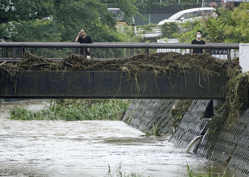 People look at debris stuck on a bridge over a river in Ninomiyamachi, southwest of Tokyo, Japan, Friday, Aug. 30, 2024, following a severe weather system in the area. (Yuya Shino/Kyodo News via AP)