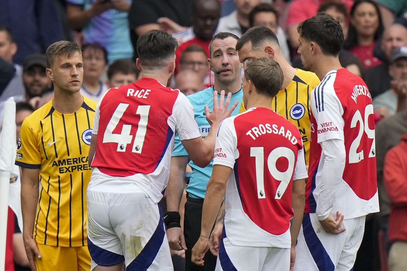 Arsenal's Declan Rice, second left, discusses with referee Chris Kavanagh, center, during the English Premier League soccer match between Arsenal and Brighton, at Emirates Stadium in London, Saturday, Aug. 31, 2024. (AP Photo/Alastair Grant)