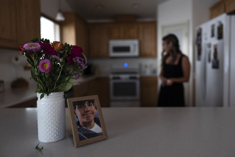 A framed photo of Elijah Ott, who died of a fentanyl overdose at 15, stands next to a vase of flowers as his mother, Mikayla Brown, works in the kitchen in Atascadero, Calif., Friday, Aug. 2, 2024. (AP Photo/Jae C. Hong)