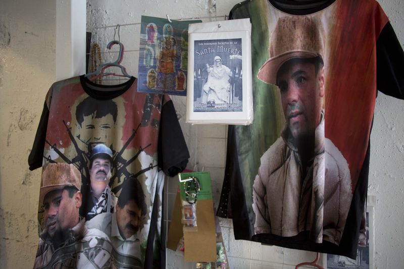 FILE - T-shirts emblazoned with images of Mexican drug lord Joaquin "El Chapo" Guzman hang for sale inside the shrine of a faith healer, in Mexico City, Oct. 16, 2015. (AP Photo/Eduardo Verdugo, File)