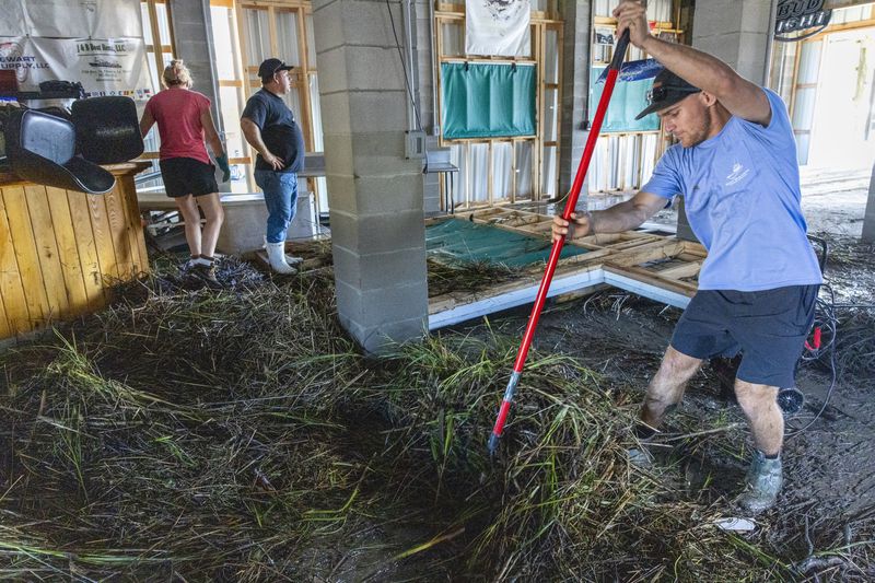 Jansen Pellegrin, right, rakes away marsh grass that floated into a living room area at his family's fishing camp from Hurricane Francine in Terrebonne Parish, La., Thursday, Sept. 12, 2024. (Chris Granger/The Times-Picayune/The New Orleans Advocate via AP)