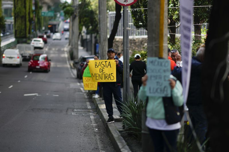 A unionized federal court worker holds a sign that reads in Spanish, "Enough of the lies" as they strike over reforms that would make all judges stand for election, outside a federal court in Mexico City, Tuesday, Aug. 20, 2024. (AP Photo/Eduardo Verdugo)