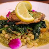 The grilled wahoo at Decatur’s Wahoo Grill rests on a bed of cherry tomatoes and lady pea ragu and is served with salsa verde and spinach. (Angela Hansberger for The Atlanta Journal-Constitution)