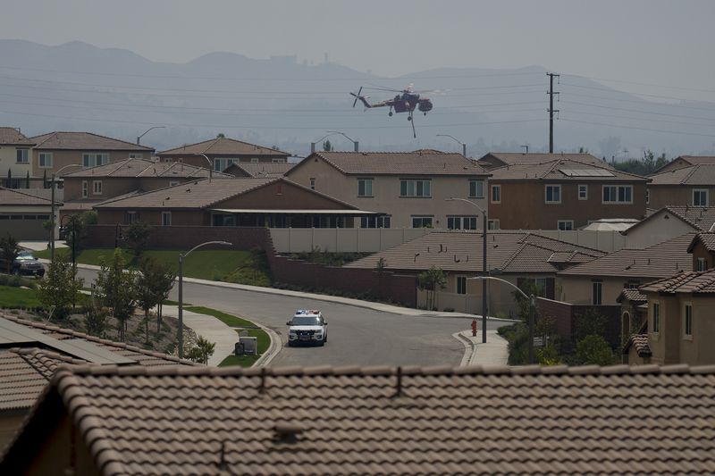 A water dropping helicopter hovers over a neighborhood as crews battle the Line Fire Saturday, Sept. 7, 2024, in Highland, Calif. (AP Photo/Eric Thayer)