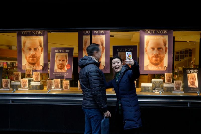 FILE - A couple take a photograph in front of a display of copies of Prince Harry's book 'Spare" in the window of a book shop in London, Tuesday, Jan. 10, 2023. (AP Photo/Kirsty Wigglesworth, File)