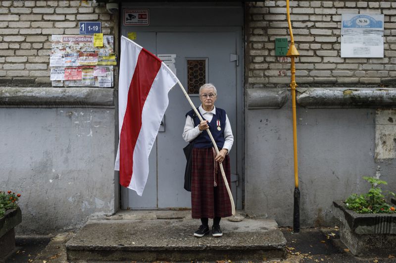 FILE - Nina Bahinskaya, 73, poses for a photo holding a flag that became the symbole of the opposition at an entrance of her apartment building in Minsk, Belarus, on Sept. 10, 2020. (AP Photo, File)