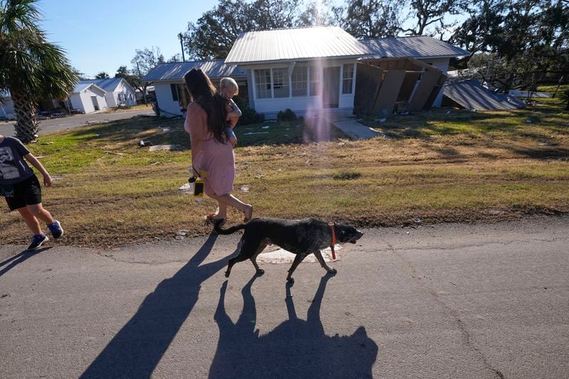 A loose dog walks past a group from St. Augustine, Fla., who did not want to give their name, that arrived to help storm victims, as they walk to pray outside the damaged First Baptist Church in the aftermath of Hurricane Helene, in Horseshoe Beach, Fla., Sunday, Sept. 29, 2024. (AP Photo/Gerald Herbert)