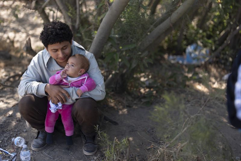 A migrant man seeking asylum sits with his baby daughter as he waits to be transported and processed, Wednesday, June 5, 2024, near Dulzura, Calif. President Joe Biden on Tuesday unveiled plans to enact immediate significant restrictions on migrants seeking asylum at the U.S.-Mexico border as the White House tries to neutralize immigration as a political liability ahead of the November elections. (AP Photo/Gregory Bull)