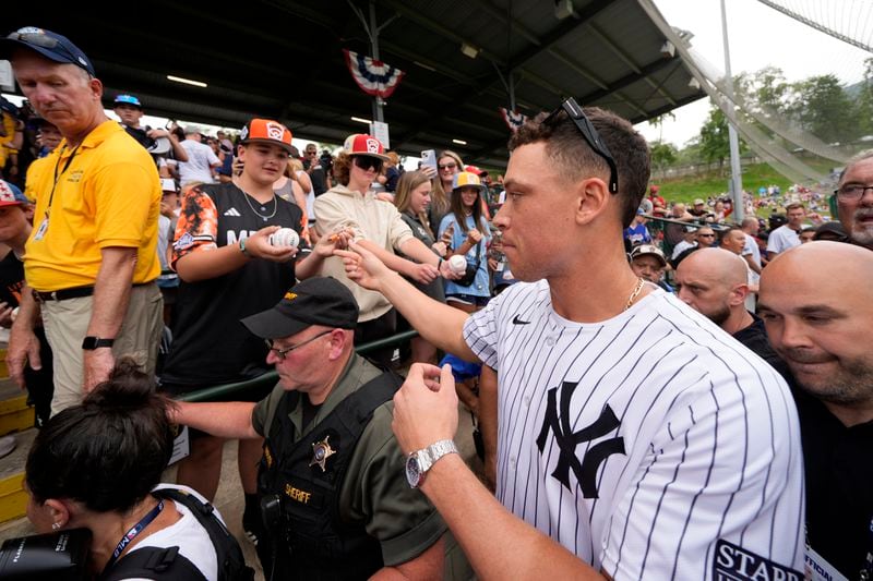 New York Yankees' Aaron Judge, right, makes his way to his seat at Lamade Stadium during a team visit to the Little League World Series tournament in South Williamsport, Pa., Sunday, Aug. 18, 2024. The Yankees will be playing the Detroit Tigers in the Little League Classic at Bowman Stadium in Williamsport, Pa., on Sunday Night Baseball. (AP Photo/Gene J. Puskar)