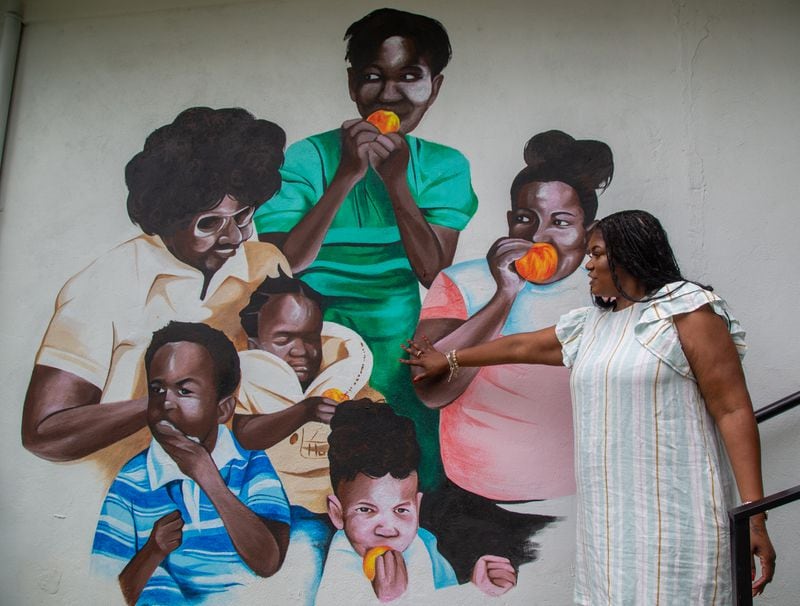 LaTonya Gates talks about the mural of her grandmother, Claudia Kemp (left) who she says raised twenty kids from the neighborhood. The mural is on the wall of the PAWkids food pantry located in Claudia's House in in Grove Park on the Westside of Atlanta. PHIL SKINNER FOR THE ATLANTA JOURNAL-CONSTITUTION.