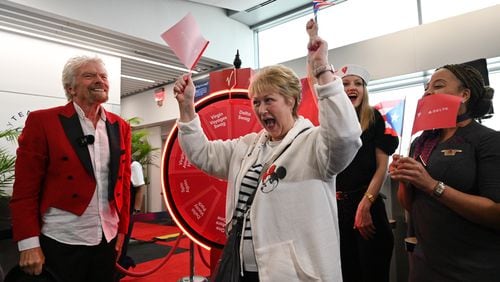 Robin Lane reacts after spinning the wheel for a prize as Richard Branson (left), founder of the Virgin Group, looks on. Virgin Voyages and Delta hosted a full departure gate takeover prior to the flight's boarding at Hartsfield-Jackson Atlanta International Airport, Thursday, Feb. 29, 2024, in Atlanta. Sir Richard Branson, Delta Air Lines and Virgin Voyages surprised customers on Delta Flight 1946 (from ATL to SJU), gifting all an-board a free cruise to celebrate all-new itineraries and the brand’s growing presence in San Juan later this year. (Hyosub Shin / Hyosub.Shin@ajc.com)