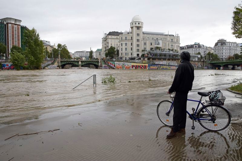 A cyclist looks at Donaukanal channel flood its banks at Urania observatory in central Vienna, Austria, Sunday, Sept. 15, 2024. (AP Photo/Heinz-Peter Bader)