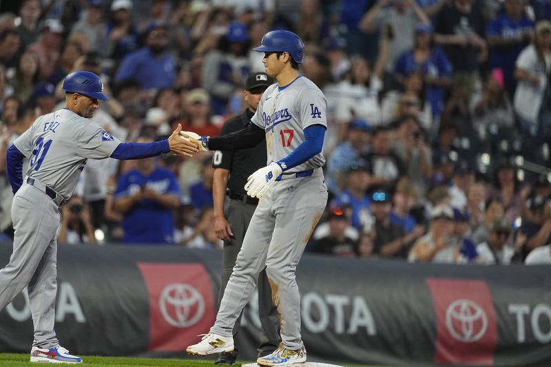 Los Angeles Dodgers third base coach Dino Ebel, left, congratulates Shohei Ohtani after he stole second base and then advance to third base on a throwing error by Colorado Rockies catcher Jacob Stallings in the second inning of a baseball game, Friday, Sept. 27, 2024, in Denver. (AP Photo/David Zalubowski)