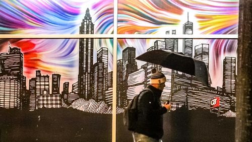With umbrella up, John Pacheco strolls by a mural of the Atlanta skyline on the QuikTrip building at 6th and Peachtree streets. Widespread rain falling Thursday morning will eventually taper off, but another round of rain could trouble the evening commute, according to Channel 2 Action News. (Credit: John Spink / John.Spink@ajc.com)