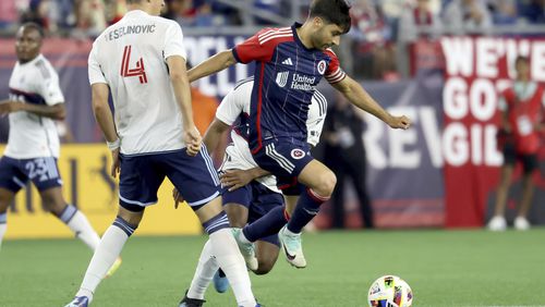 New England Revolution midfielder Carles Gil, right, dribbles between Vancouver Whitecaps defenders including Ranko Veselinovic (4) during the second half of an MLS soccer match Saturday, June 15, 2024, in Foxborough, Mass. (AP Photo/Mark Stockwell)