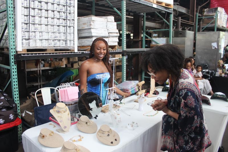 A vendor smiles as a customer admires displayed jewelry for sale at the Vegan Social event in East Point, Ga.