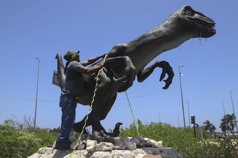 A worker secures a dinosaur statue at a theme park ahead of Hurricane Beryl's expected arrival in Chicxulub, Mexico, Thursday, July 4, 2024. (AP Photo/Martin Zetina)