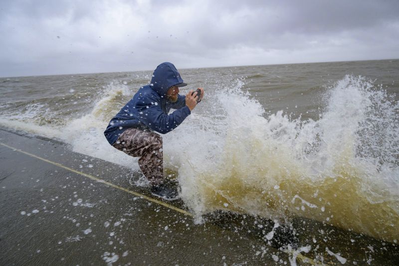 Conrad Bach gets doused with lake water while looking at waves from the wind and rain from Hurricane Francine along Lakeshore Drive along Lake Ponchartrain in New Orleans, Wednesday, Sept. 11, 2024. (AP Photo/Matthew Hinton)