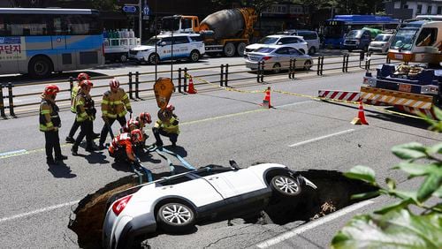 South Korean firefighters prepare to lift a vehicle that fell into a sinkhole on a street in Seoul, South Korea, Thursday, Aug. 29, 2024. (Seo Dae-yeon/Yonhap via AP)