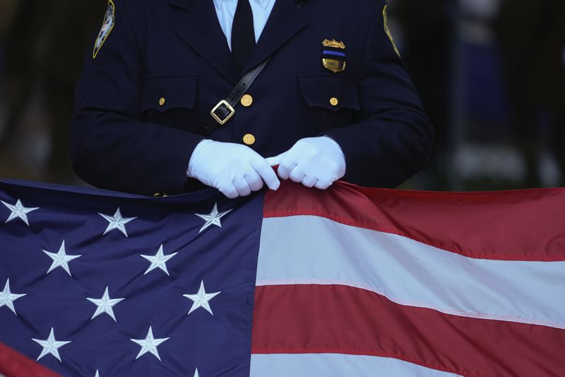 A New Jersey police officer holds an American Flag before the start of the ceremony at the 9/11 Memorial on the 23rd anniversary of the Sept. 11, 2001 terror attacks, Wednesday, Sept. 11, 2024, in New York. (AP Photo/Pamela Smith)