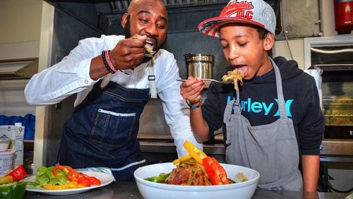 Chef Cheikh Ndiaye teaches 12-year-old Fallou Diouf (who is half Senegalese) to cook some of the national dishes of his father’s homeland in the kitchen of Project Community Connections Inc. recently. Here, they are taking a first bite of the Chicken Yassa. CONTRIBUTED BY CHRIS HUNT PHOTOGRAPHY