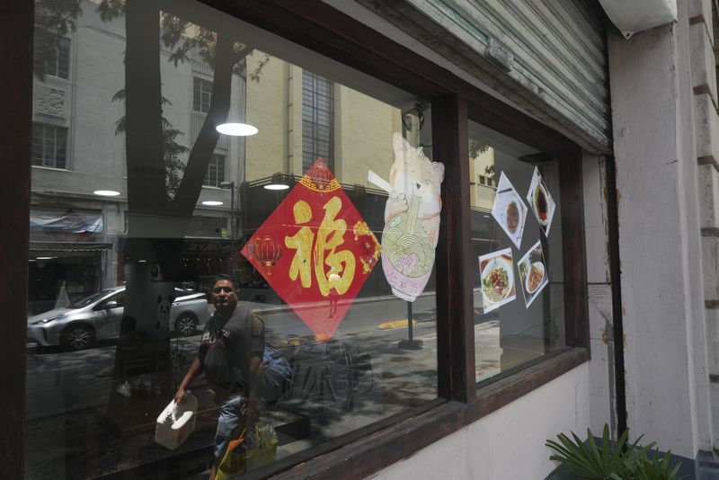 A pedestrian is reflected in the storefront window of a restaurant in Chinatown, in Mexico City's historic center, Saturday, June 8, 2024. (AP Photo/Fernando Llano)