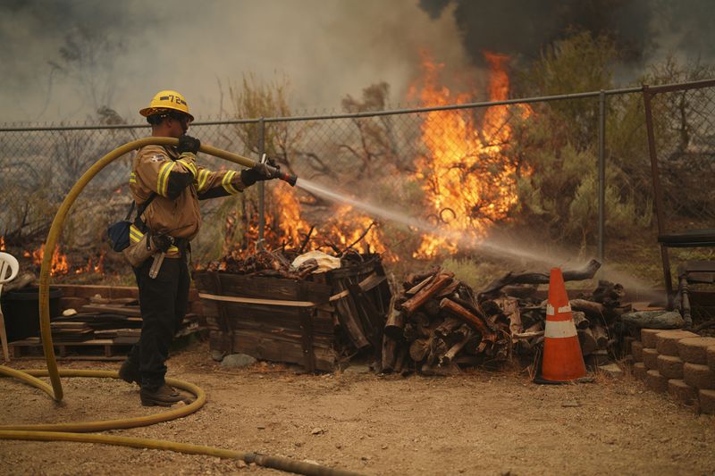 A firefighter douses flames in the perimeter of a property while battling the Bridge Fire Wednesday, Sept. 11, 2024, in Wrightwood, Calif. (AP Photo/Eric Thayer)