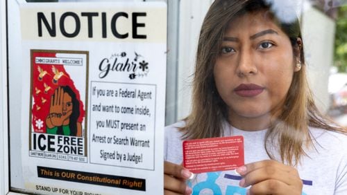 Leslie Palomino, holding “a know your rights" card, poses for a portrait at her home in Gwinnett County on Friday, July 5, 2024. Her door has a sign that states federal agents cannot enter without a warrant signed by a judge. (Arvin Temkar / AJC)