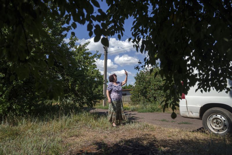 A local woman tries to find a signal for her phone before she leaves her home during evacuation to safe areas, in Toretsk, Donetsk region, Ukraine, Friday, June 28, 2024. (AP Photo/Evgeniy Maloletka)
